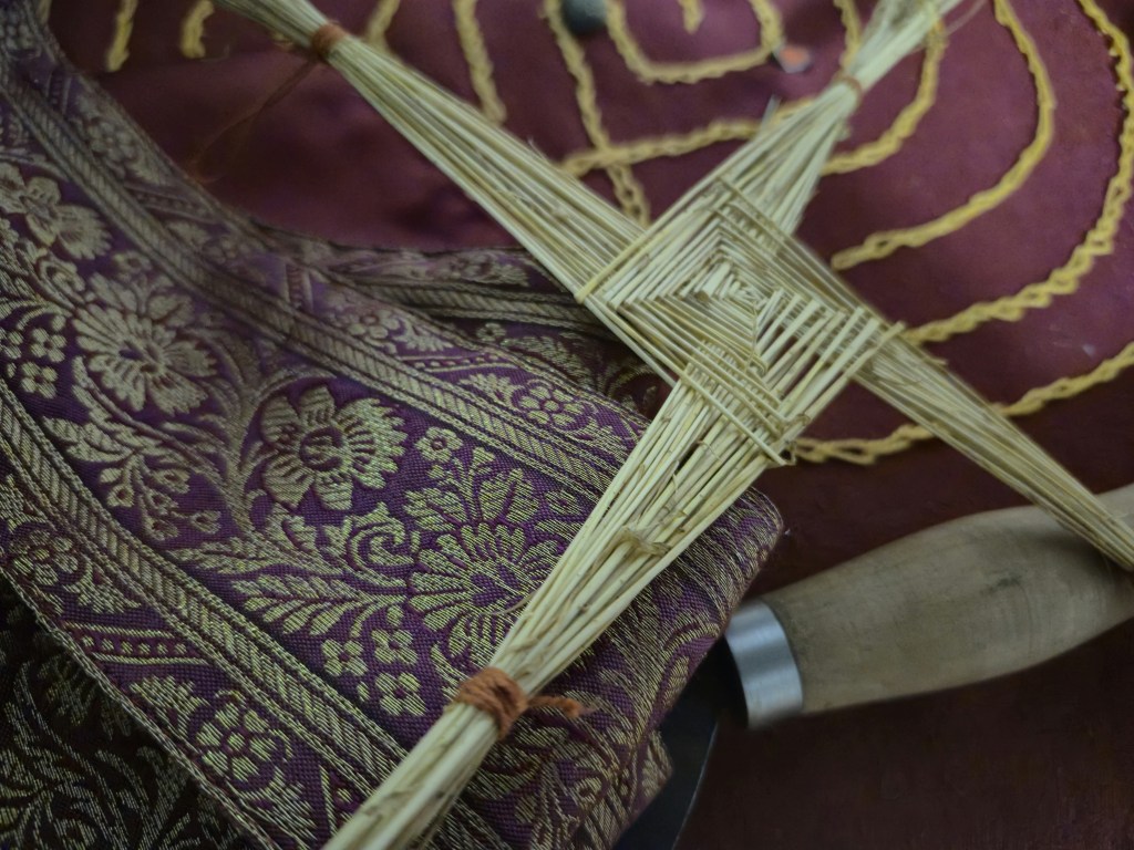 Brigid's cross in straw on a cloth background. There's a floral motif in gold on burgundy cloth.