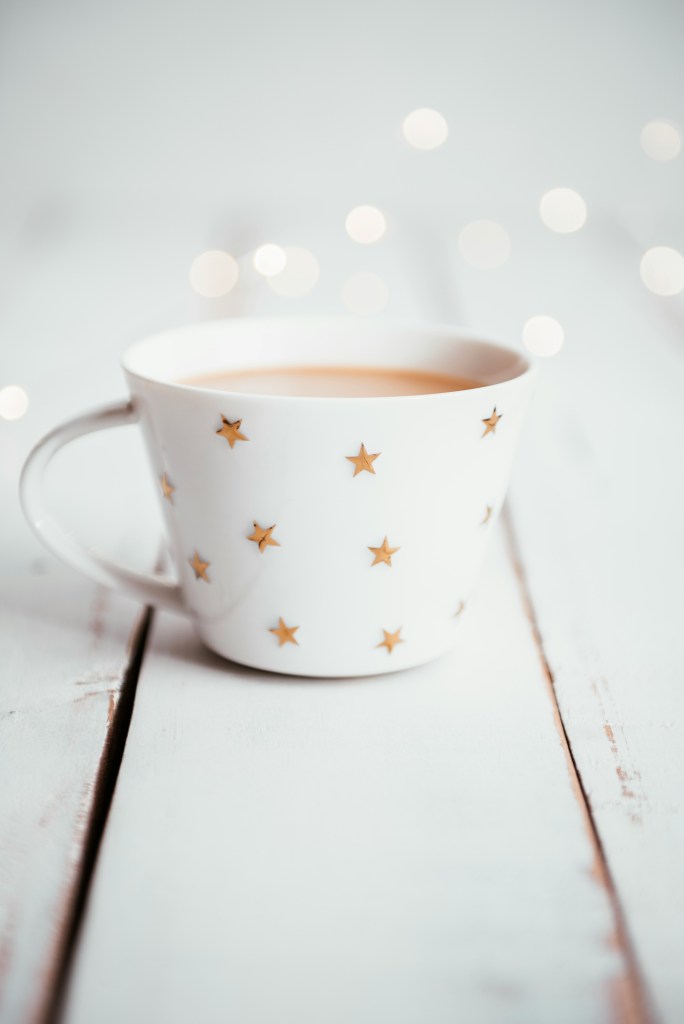 A simple white mugs with gold stars. Tea with milk inside. White background with the suggestion of lights or glitter.