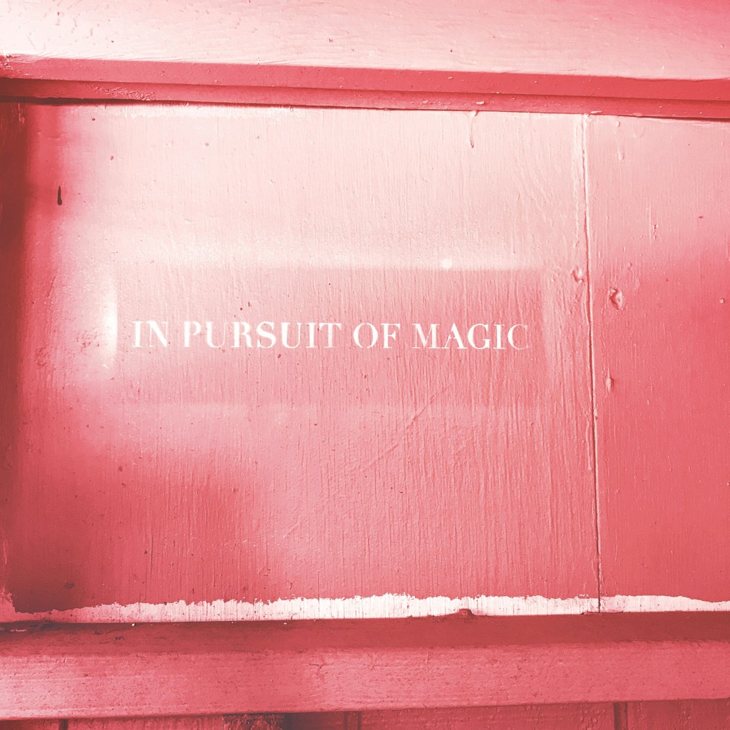 A pink wall with "In Pursuit of Magic"  stencilled in white. 